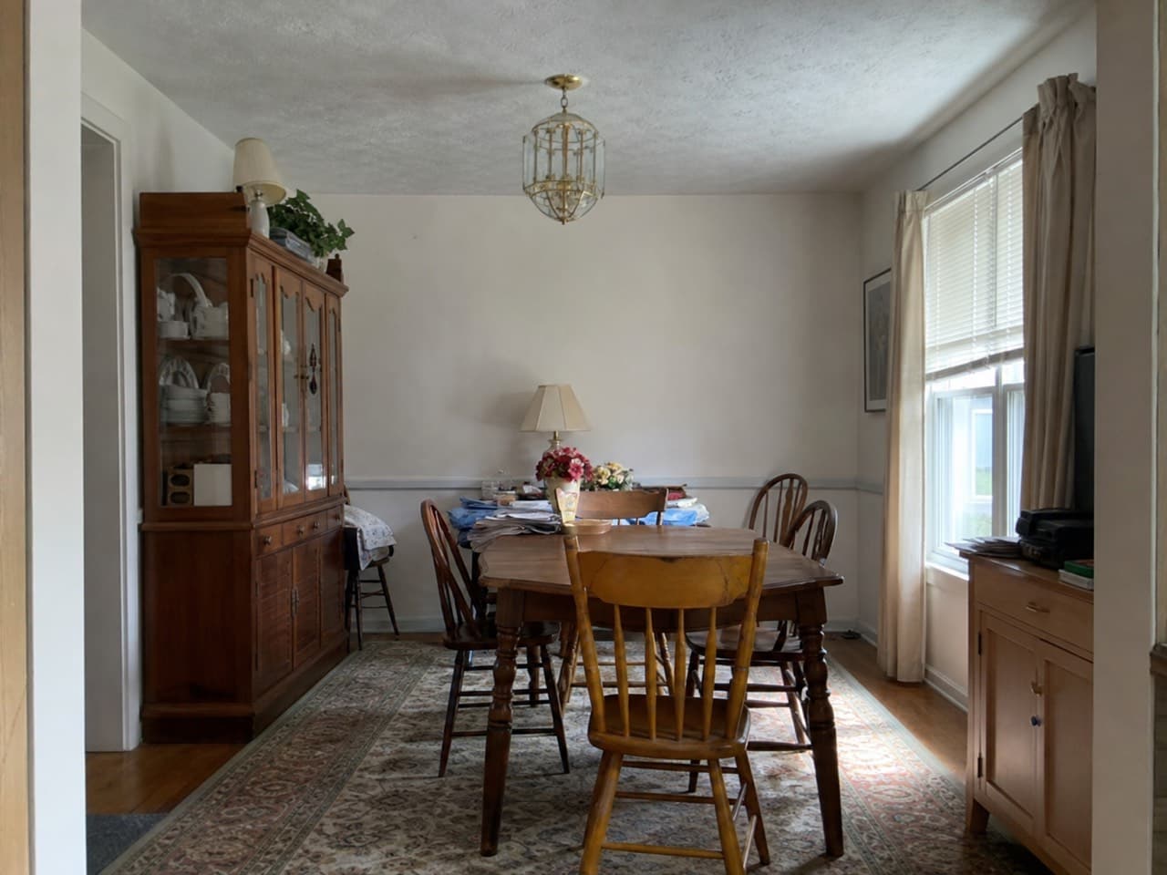 A furnished dining room with a table, chairs, a hutch and clutter