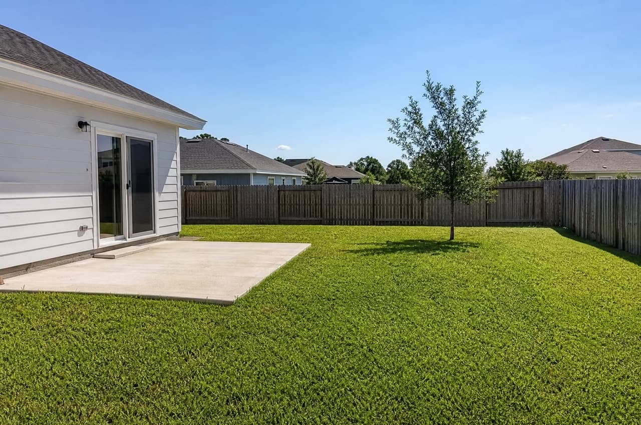 A plain backyard with a bare lawn and concrete patio before AI redesign